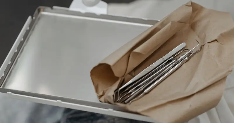 Close-up of dental tools wrapped in brown paper on a metal tray, highlighting dental care readiness.